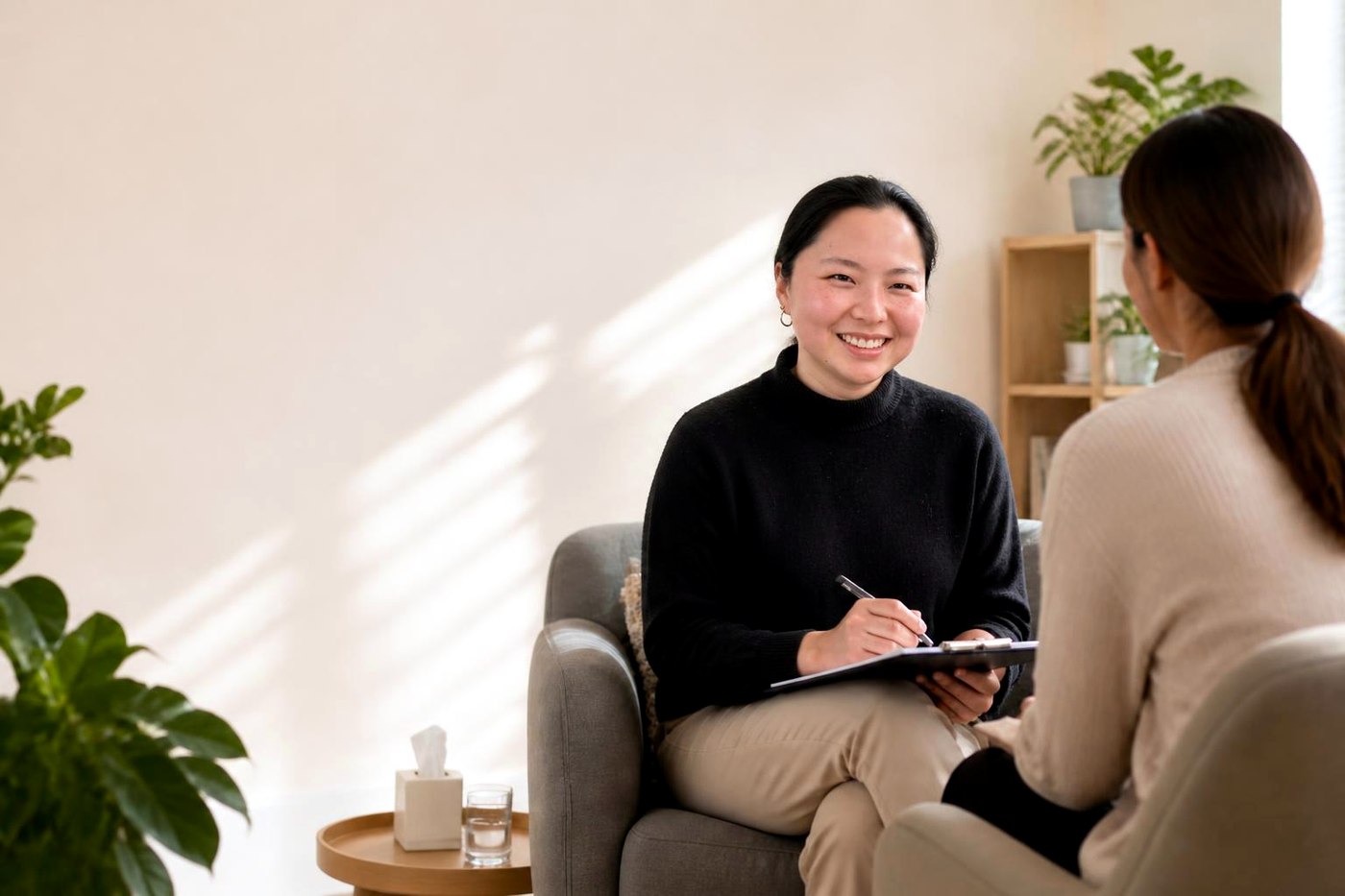 An Allied Pathways clinician smiling warmly while taking notes during a home consultation with a client